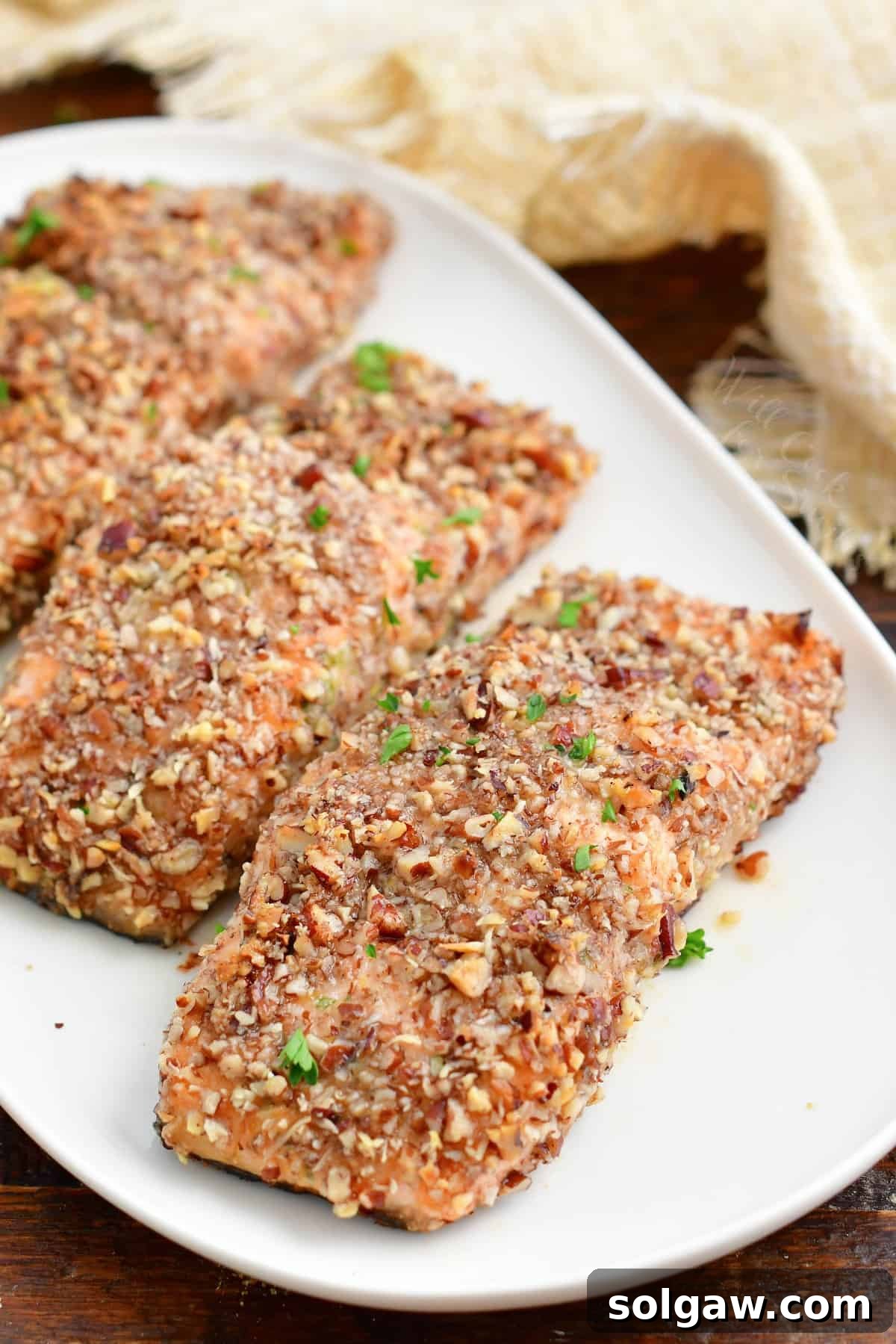 Pecan crusted salmon fillets, beautifully golden and ready to eat, are artfully arranged on a pristine white plate.