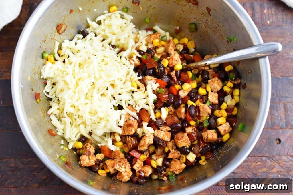 Zesty Southwest Chicken Zucchini Boats 8 Adding shredded pepper jack cheese to the vibrant Southwest chicken filling in a metal mixing bowl.