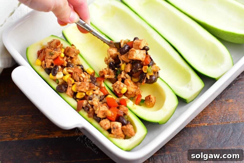 Zesty Southwest Chicken Zucchini Boats 9 Adding generous scoops of Southwest chicken filling into the hollowed zucchini boats in a baking dish.