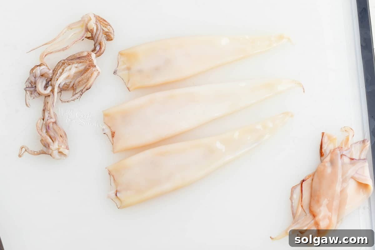 three squid cleaned with tentacles, body and fins on the board