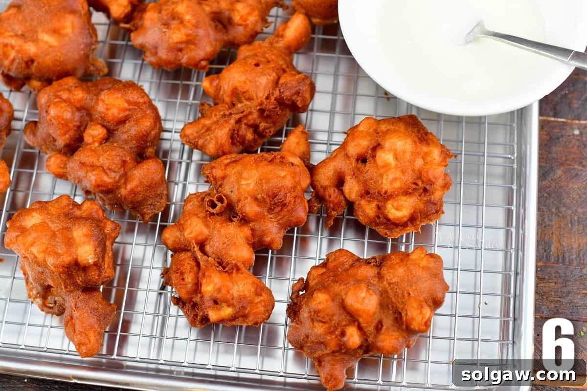 Golden Apple Delights 6 Fried apple fritters on a wire rack, with glaze drizzled over them.
