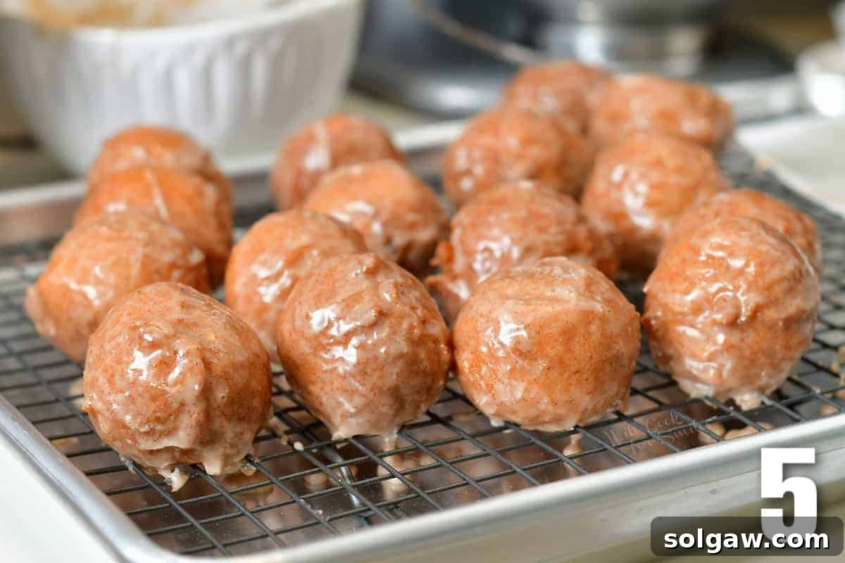 Glazed pumpkin donut holes laid out on a wire rack fitted in a baking sheet.