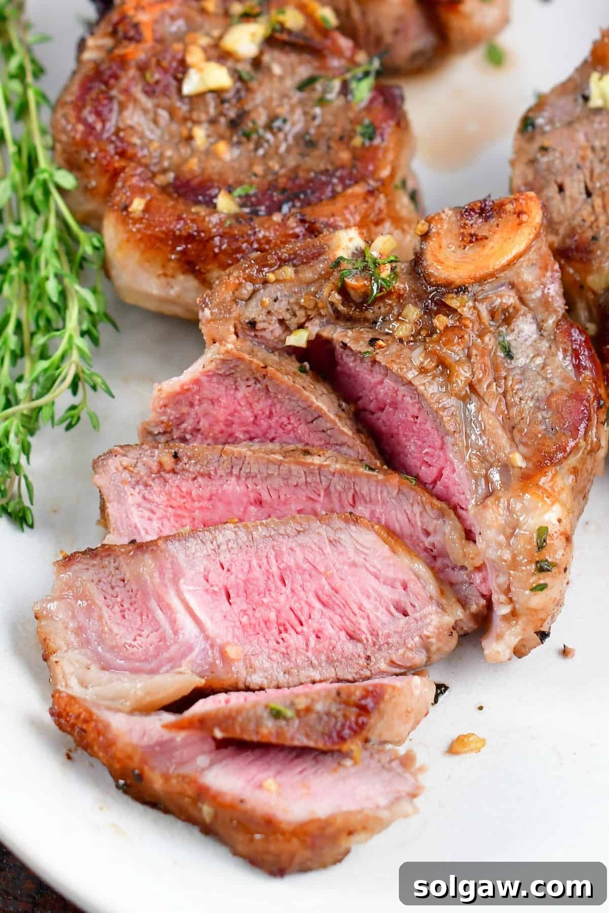 Close-up of perfectly sliced lamb chops on a white plate, revealing their tender, juicy interior.