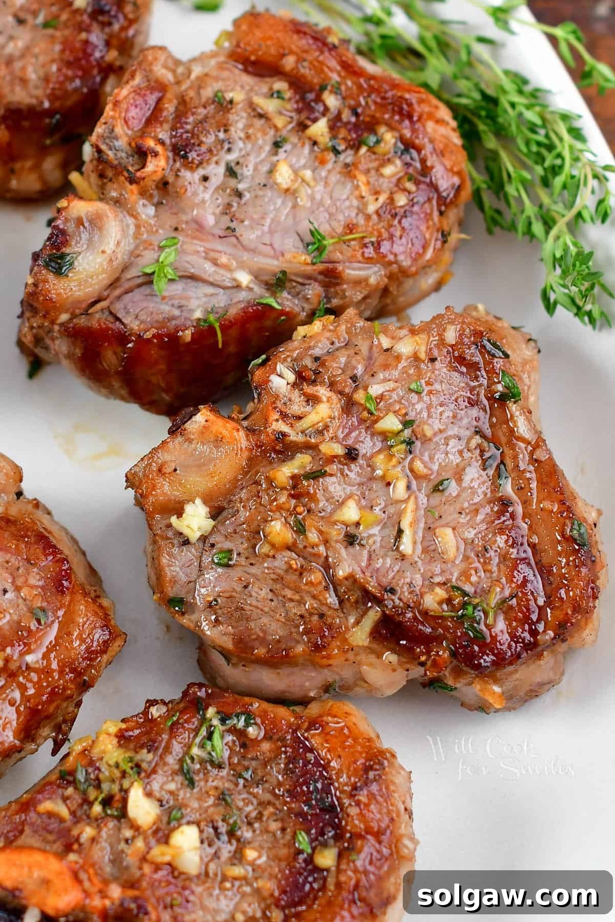 A few perfectly seared lamb chops on a plate, garnished with fresh thyme sprigs.