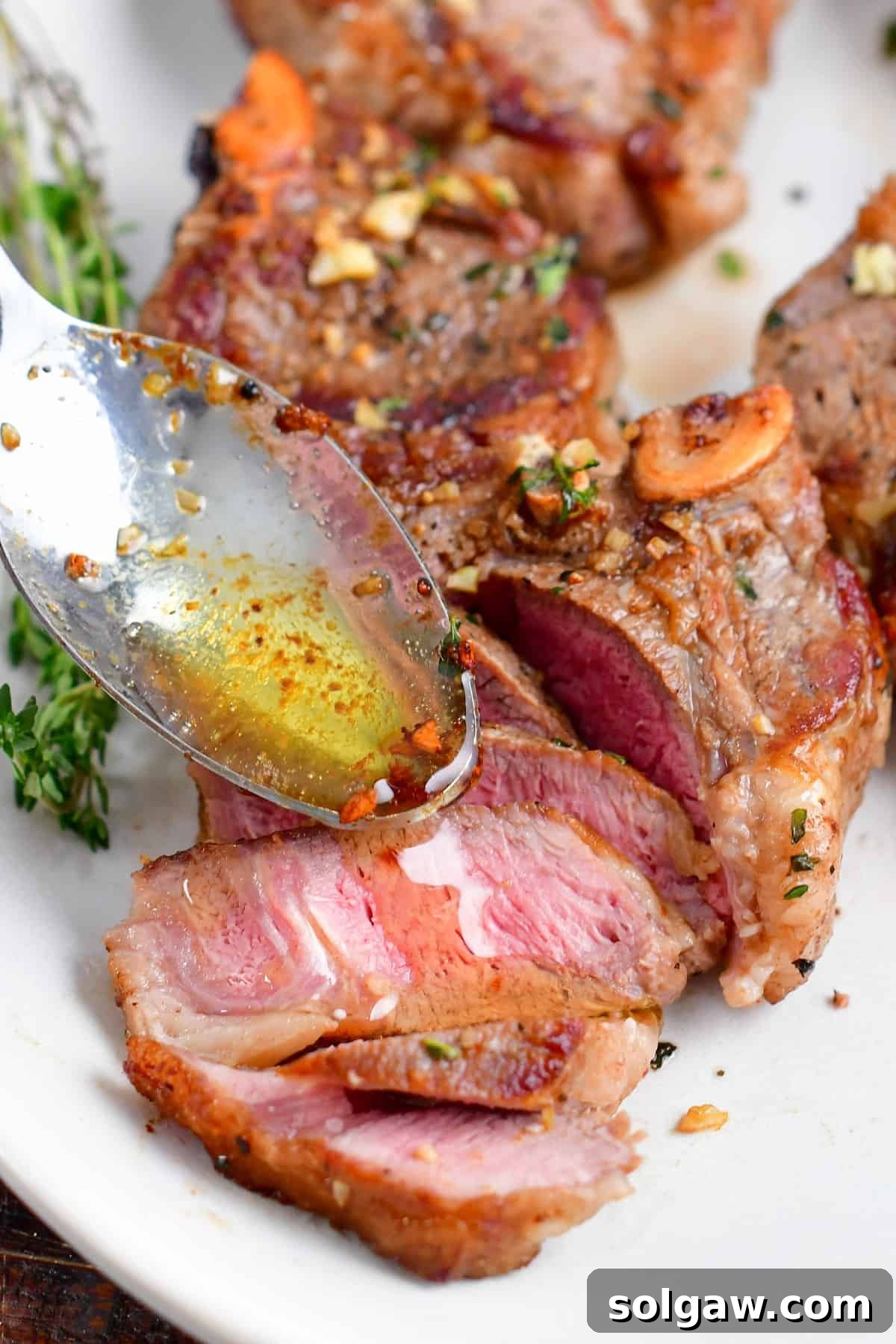 A spoon drizzling rich butter sauce over a perfectly sliced lamb chop on a plate.