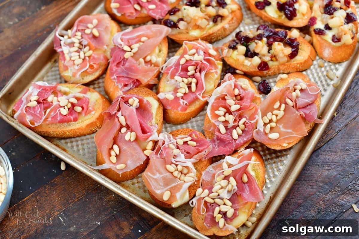 crostini on a sheet pan topped with prosciutto and pine nuts