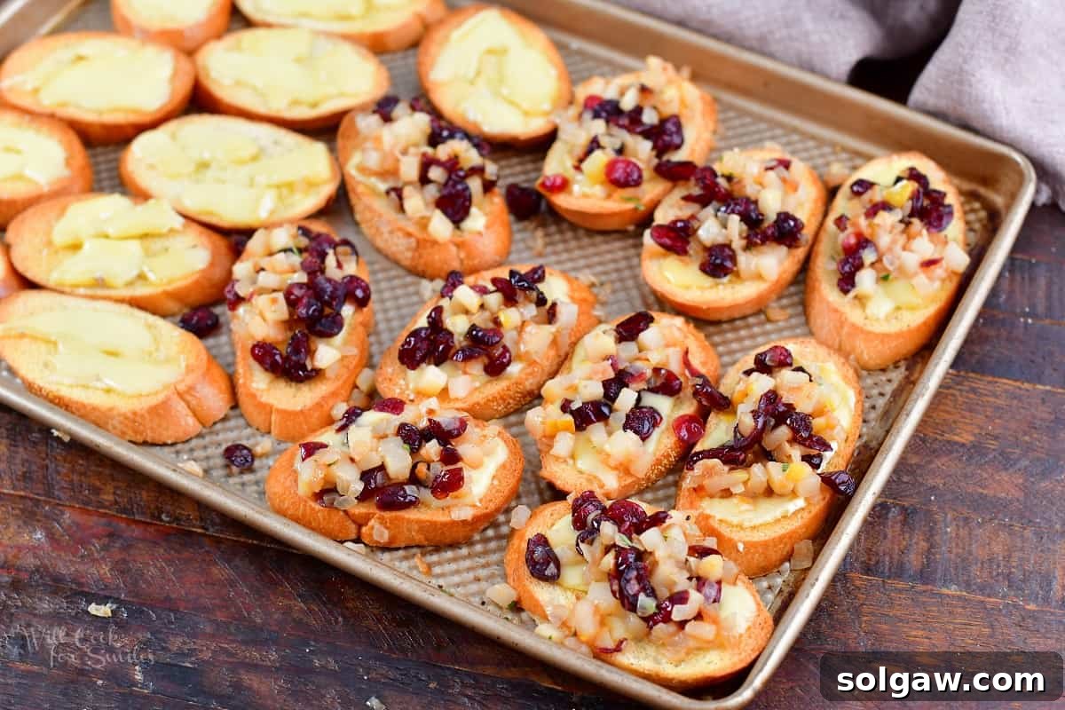 crostini on the baking sheet topped with cranberry pear