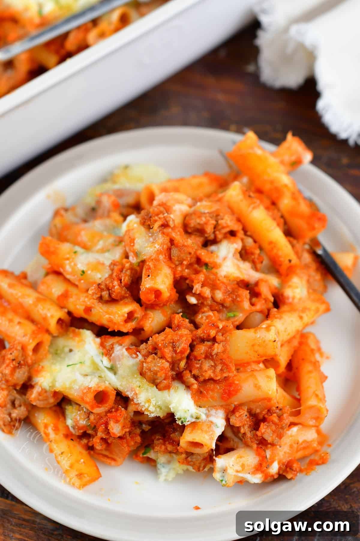 A plate of baked ziti with meat sauce, garnished with fresh basil, and a fork ready to enjoy.