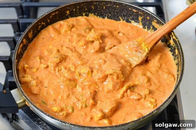 Butter Chicken Murgh Makhani 11 Finished butter chicken stewing in its vibrant orange, creamy sauce in a large cooking pan.