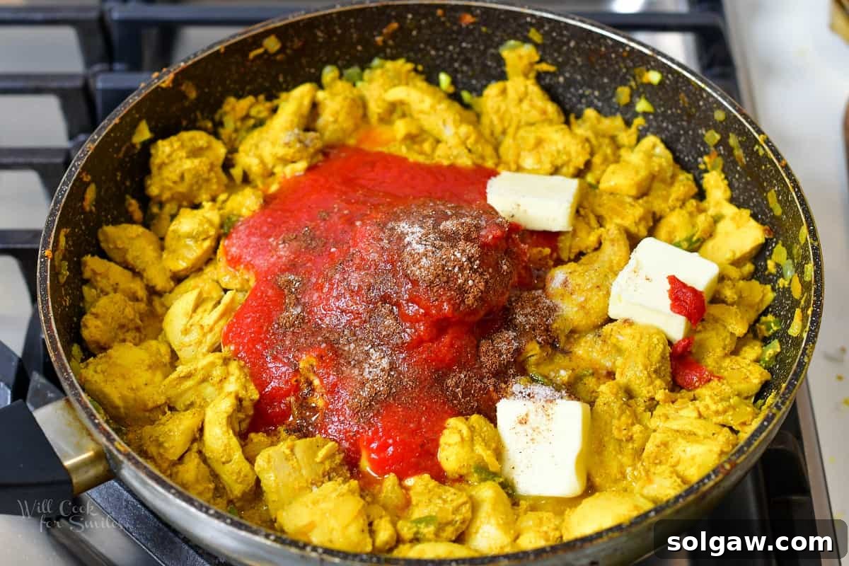 Butter Chicken Murgh Makhani 9 Adding rich tomato sauce, aromatic spices, and a knob of butter to the cooked chicken in a pan, ready to simmer.