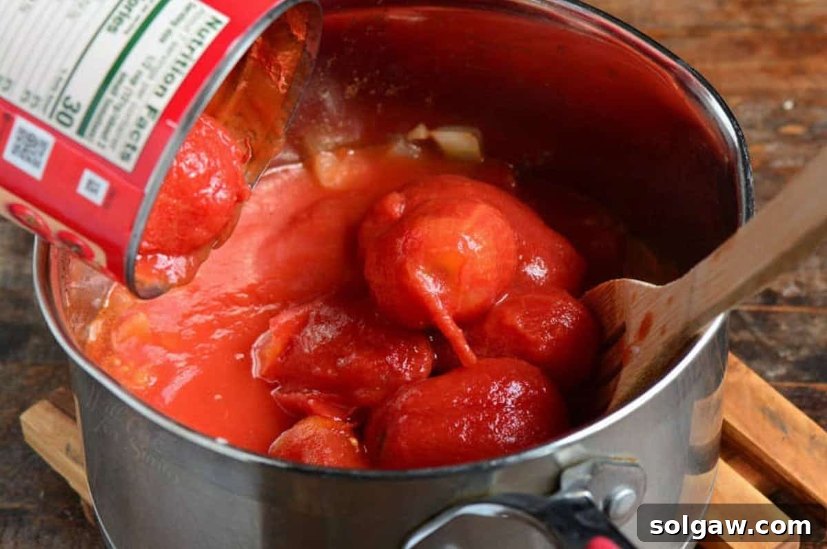 Adding ripe, red whole tomatoes into a large cooking pot, with a wooden spoon resting nearby, ready to stir.
