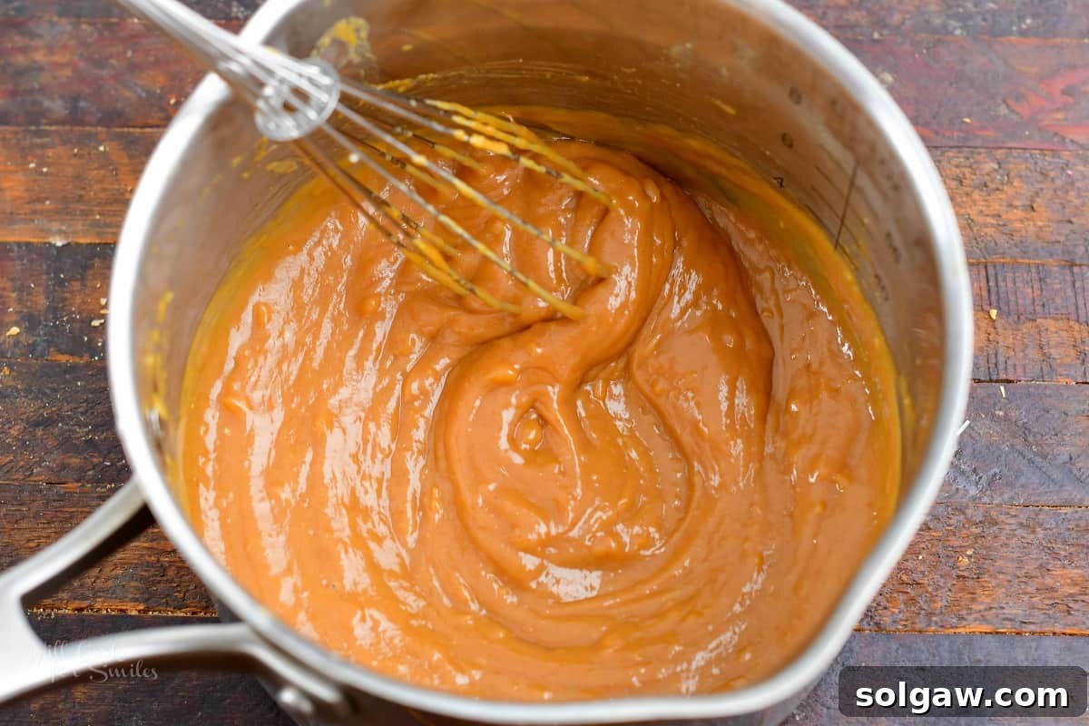 A hand whisking the peanut sauce ingredients together in a small saucepan over low heat, ensuring a smooth and creamy consistency.