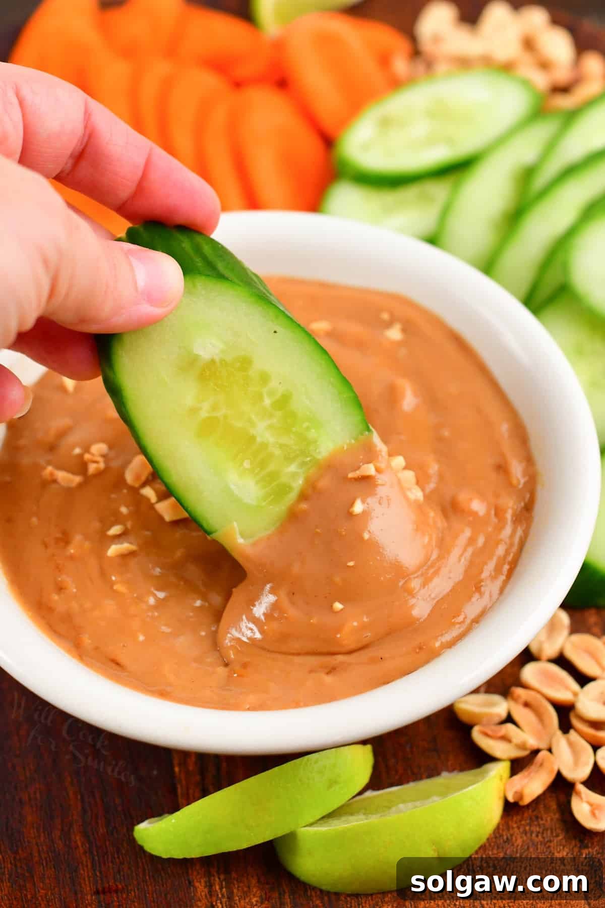 Cucumber being dipped into homemade peanut sauce, illustrating a serving suggestion.