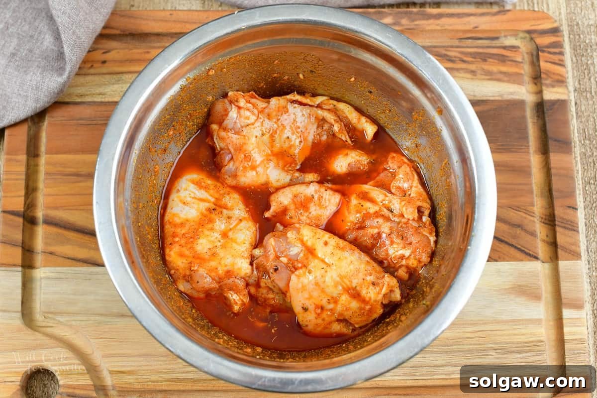 Zesty Air-Fried Southwest Chicken Thighs 4 Raw chicken thighs coated generously in Southwest marinade within a mixing bowl.