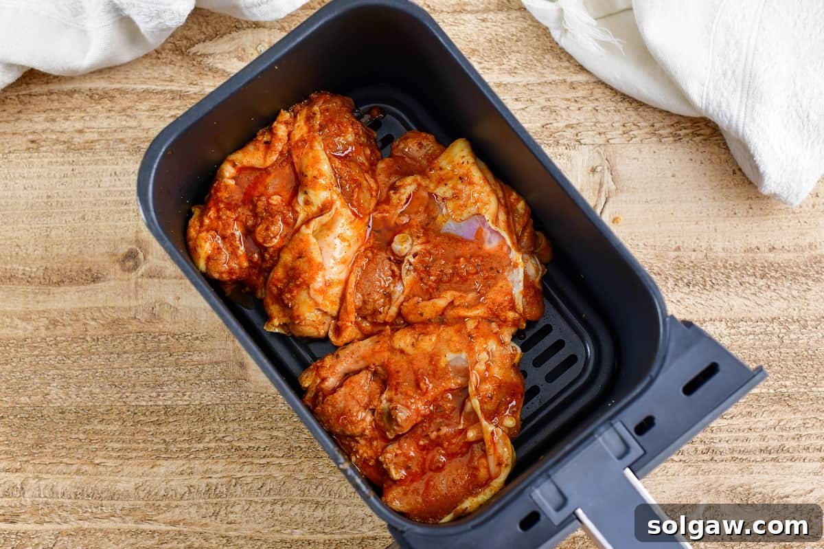 Zesty Air-Fried Southwest Chicken Thighs 5 Marinated chicken thighs arranged in a single layer in an air fryer basket, ready for cooking.