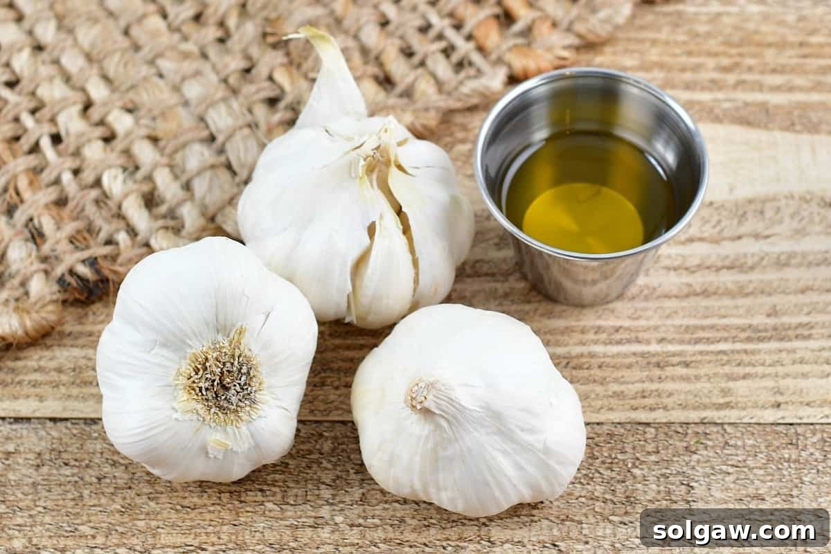 Sweet Mellow Roasted Garlic 3 Three garlic cloves, ready for roasting, with olive oil in a small cup, symbolizing the simple ingredients needed.
