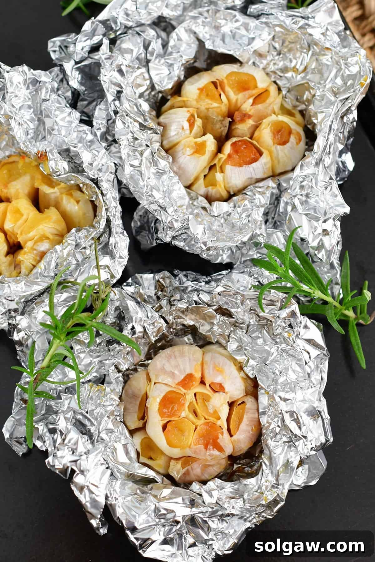Sweet Mellow Roasted Garlic 6 Three individual cloves of roasted garlic, each carefully wrapped in aluminum foil, ready for storage or use.
