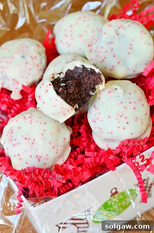 Exquisitely presented Peppermint Oreo Bites in a decorative gift box, nestled on a bed of red shredded paper, with one bite enticingly placed on top, ready to be enjoyed.