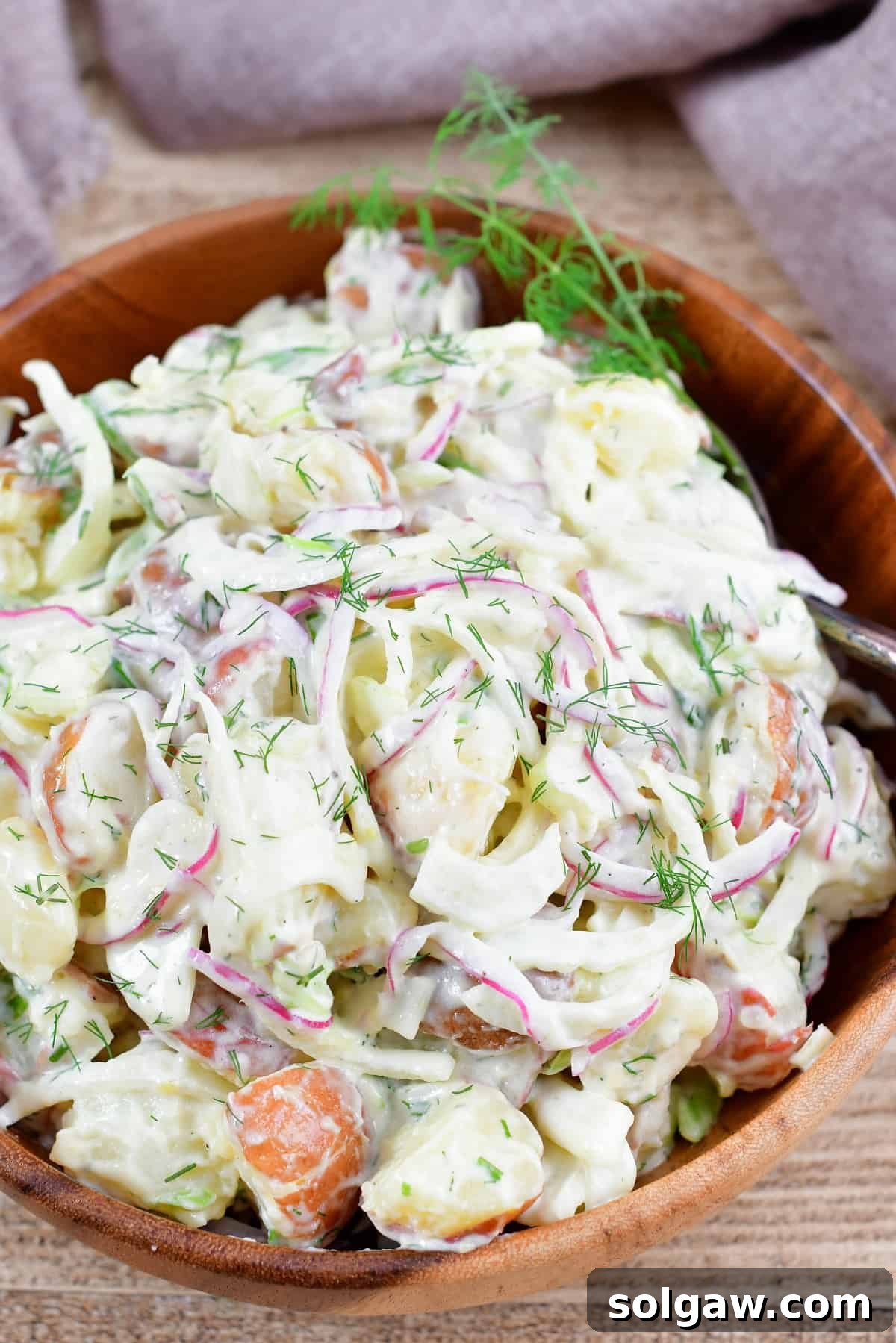 A close-up of creamy Fennel Potato Salad served in a rustic wooden bowl, garnished with fresh dill.