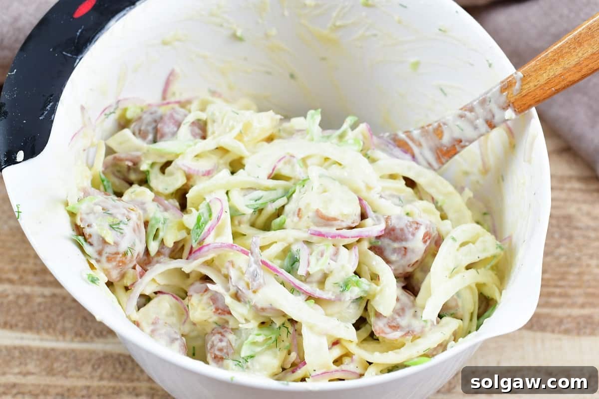 Mixing the creamy fennel potato salad in a large white mixing bowl with a spatula.