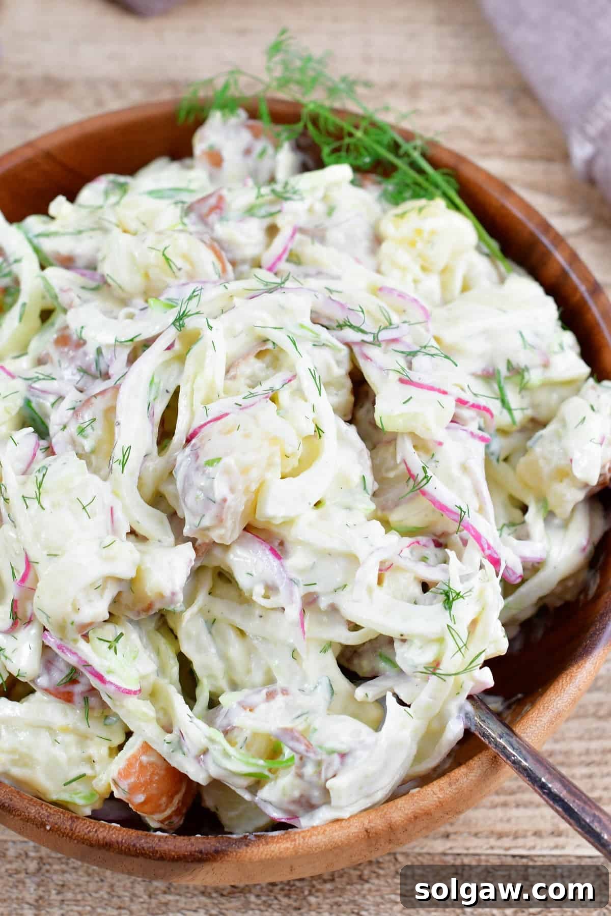 Scooping out a portion of the freshly mixed fennel potato salad from the bowl into a serving dish.