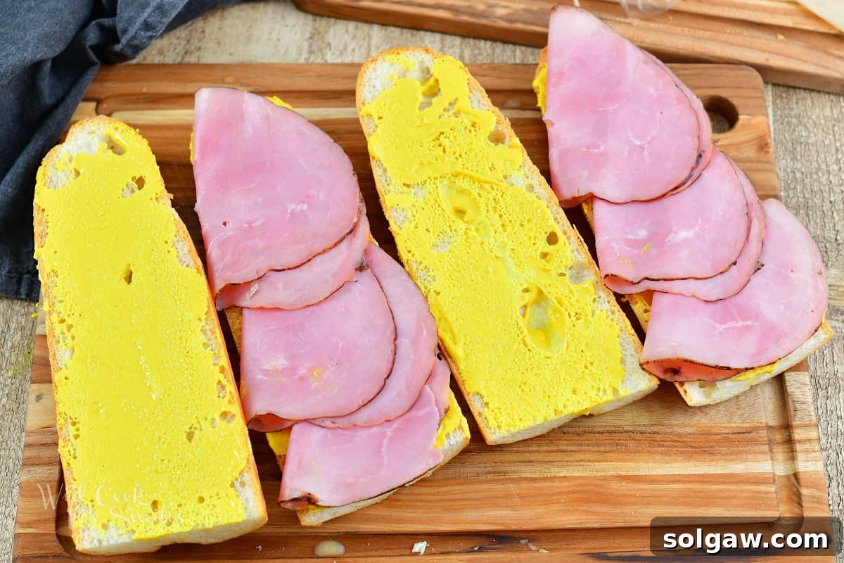 four slices of bread with mustard and ham on two, ready for the next layer