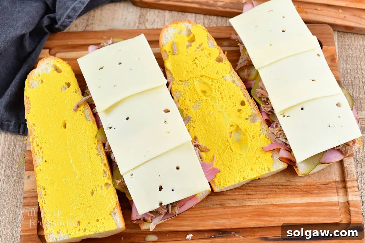 four sliced pieces of long bread with mustard and meats on two with cheese for Cuban sandwiches