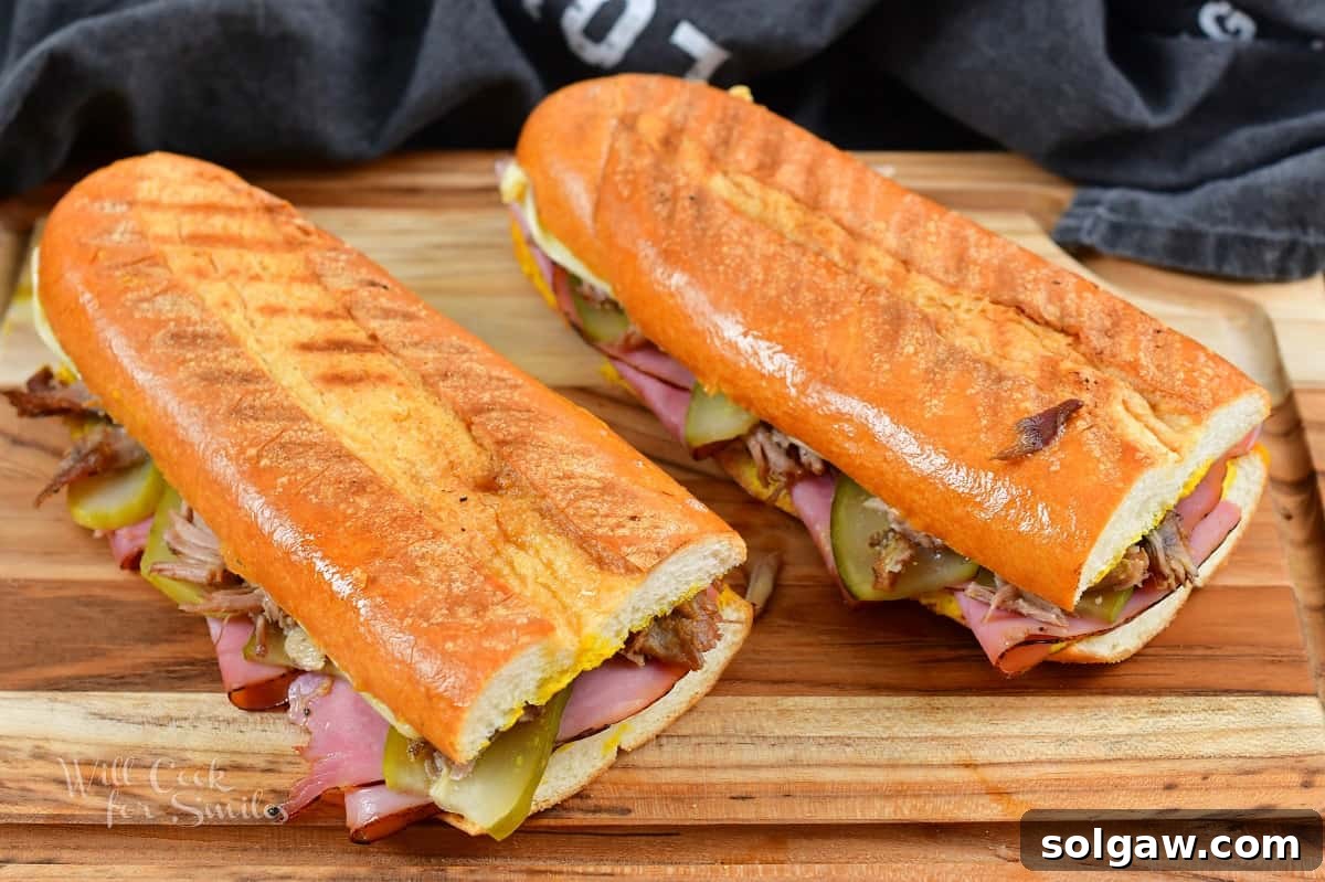 two long cooked Cuban sandwiches on the board, cut in half