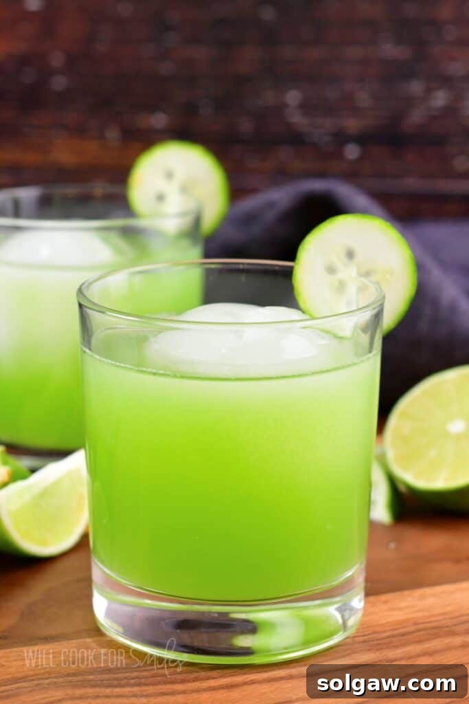 Closeup of a bright green cucumber cocktail with ice and a cucumber slice garnish.