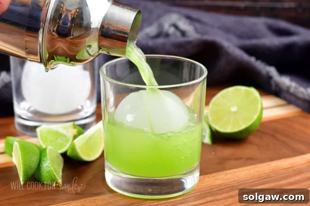 Pouring the bright green cucumber cocktail over fresh ice into a glass.