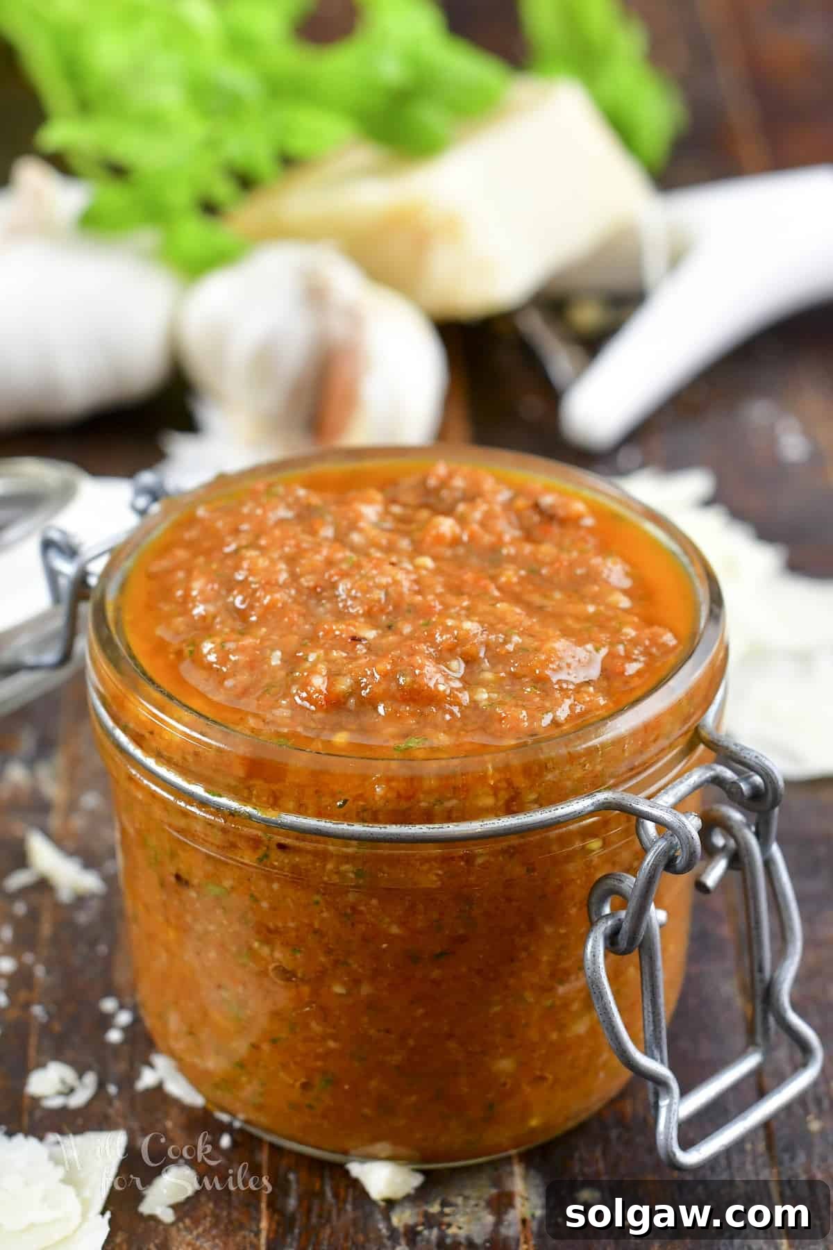 Closeup of vibrant red sun-dried tomato pesto in a clear glass jar, ready to be served or stored.