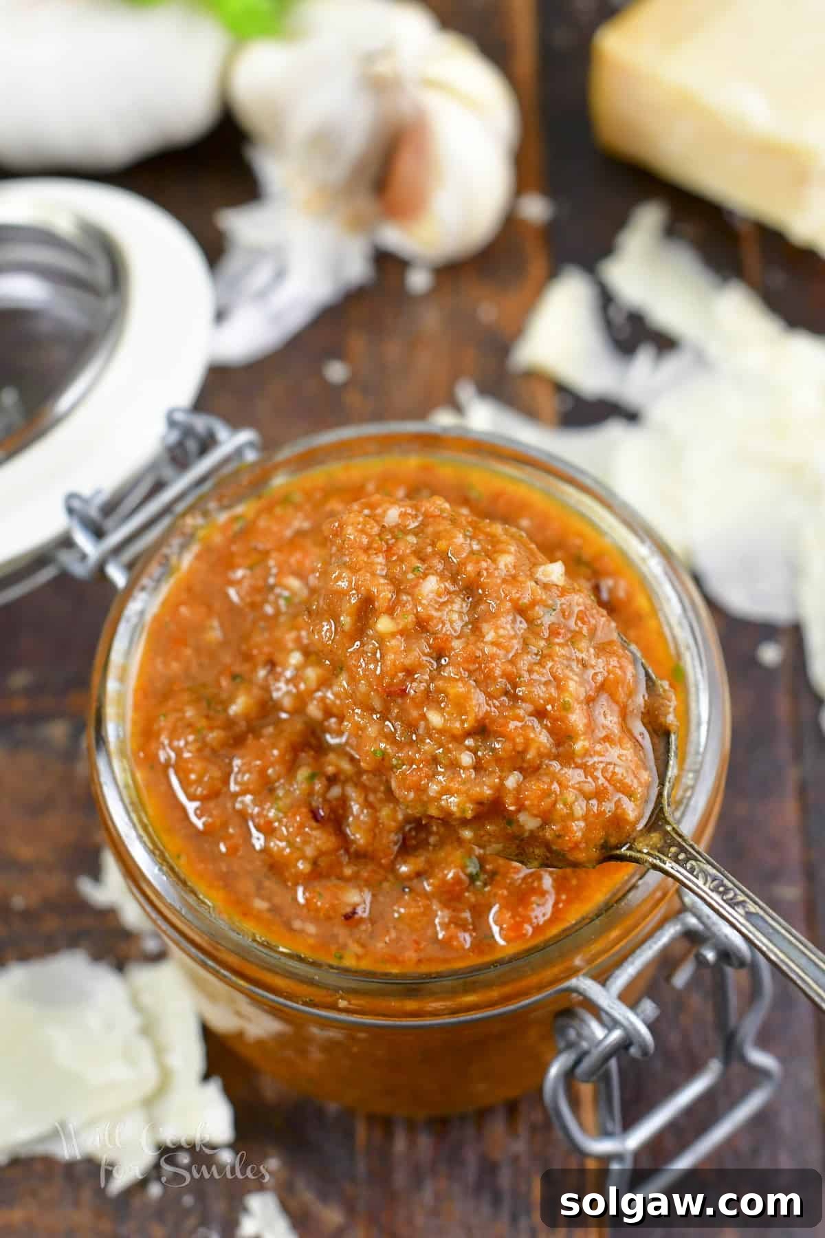 Scooping rich, red pesto rosso from a glass jar with a spoon.