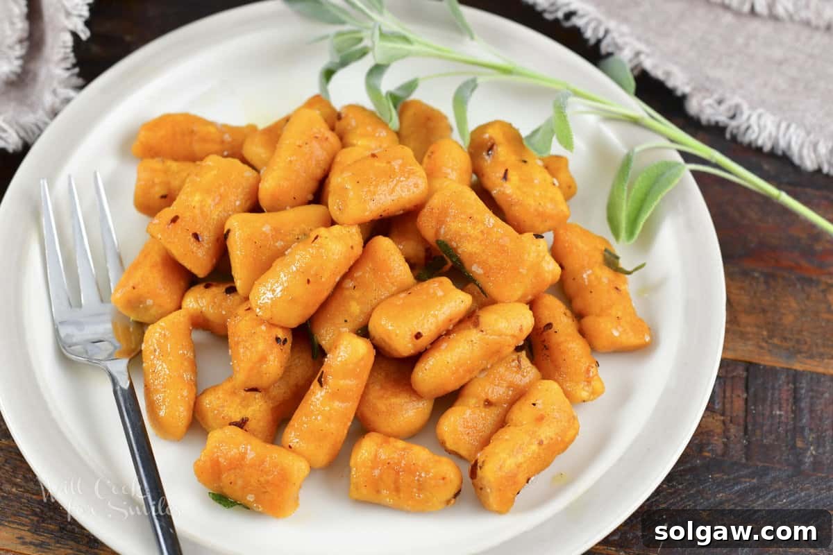Close-up of cooked sweet potato gnocchi sautéed in butter with fresh sage and red pepper flakes, in a skillet.