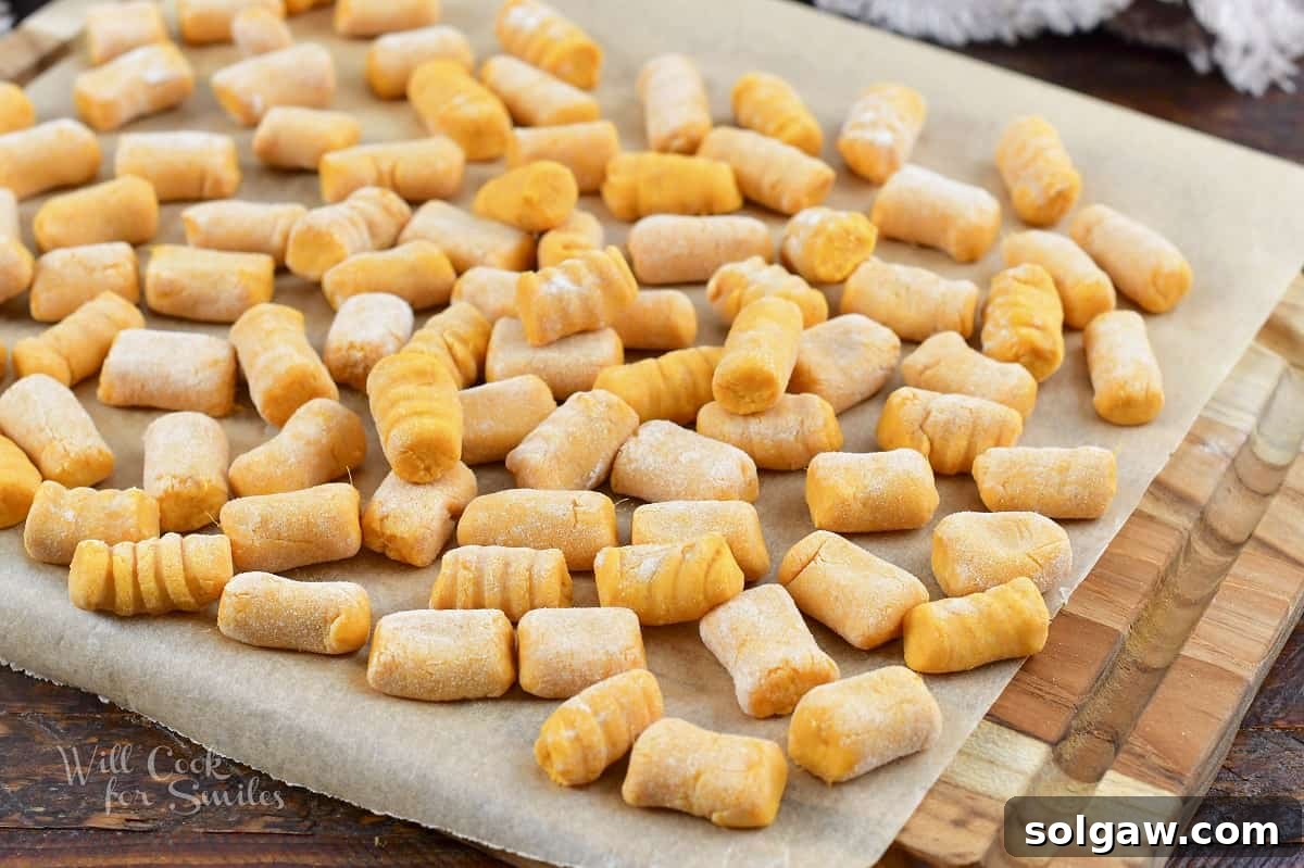 Individual sweet potato gnocchi pieces spread out evenly on parchment paper, ready for freezing.