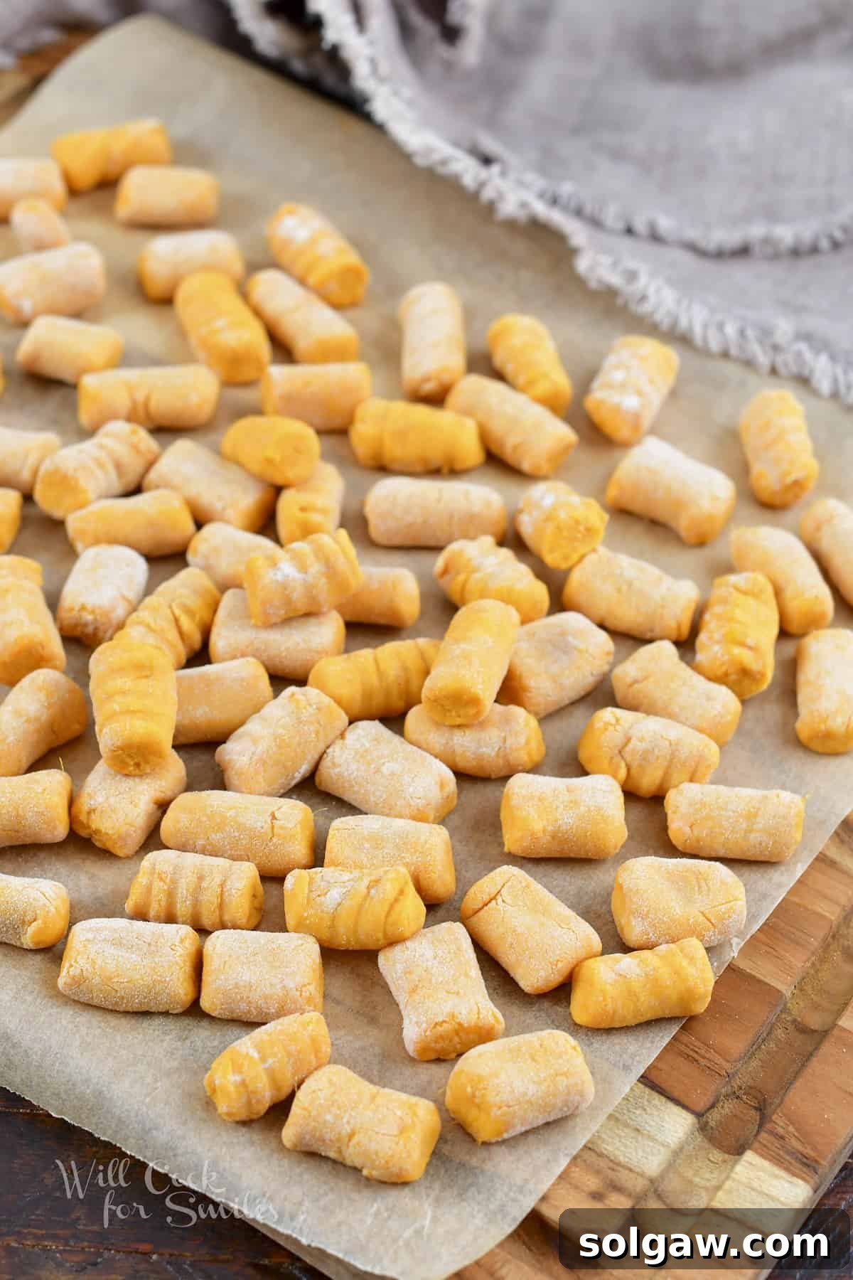 Close-up of uncooked sweet potato gnocchi pieces neatly arranged on a wooden cutting board.