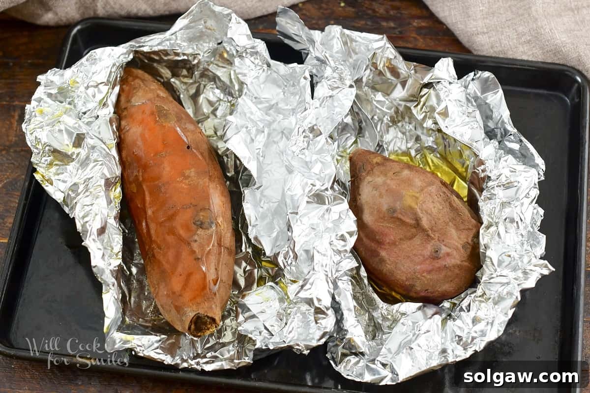 Two large baked sweet potatoes, still wrapped in foil, fresh out of the oven.
