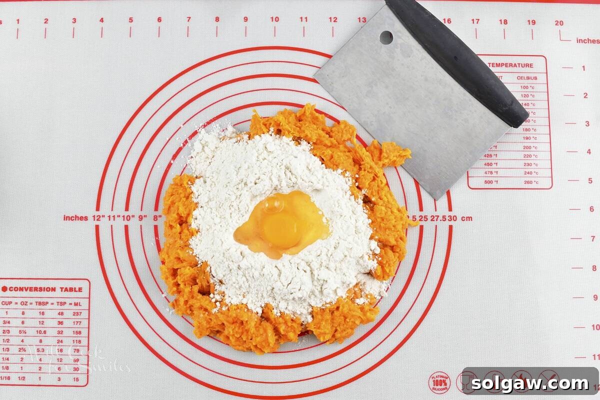 Mashed sweet potato formed into a mound on a work surface, with flour and an egg added, ready for mixing.