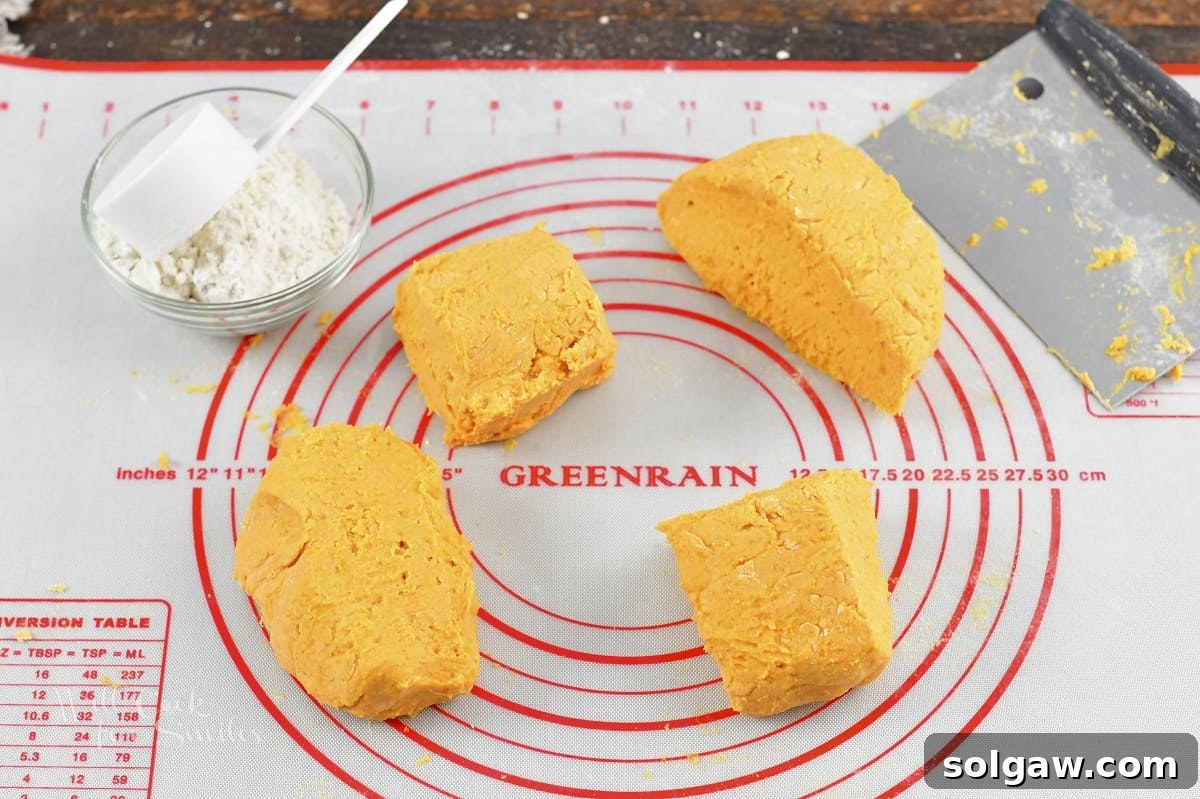 Sweet potato gnocchi dough divided into four equal pieces, alongside a small bowl of flour.