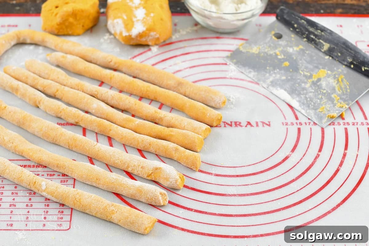 Rolled logs of sweet potato gnocchi dough on a floured surface, ready to be cut into individual pieces.