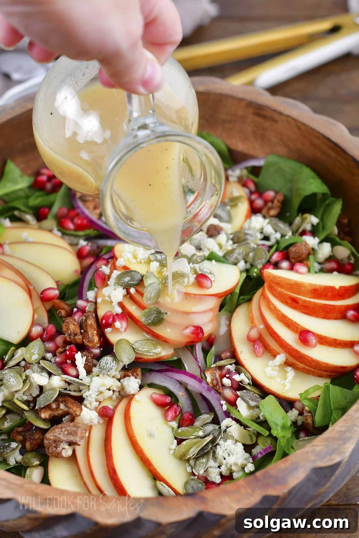 Orchard Apple Bliss 6 A hand pouring homemade apple cider vinaigrette over a bowl of apple salad.