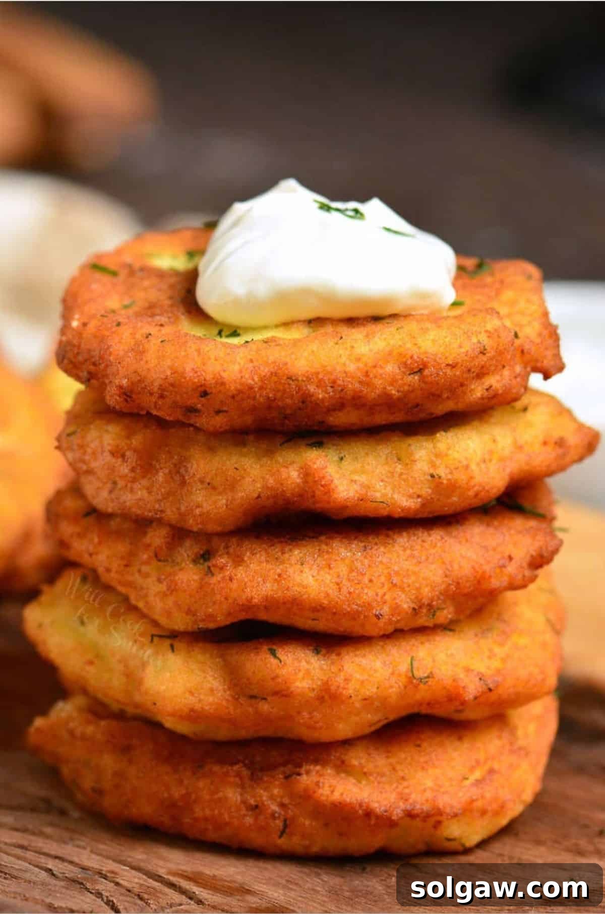 Potato pancakes on stacked on a wood surface with a dollop of sour cream on top.