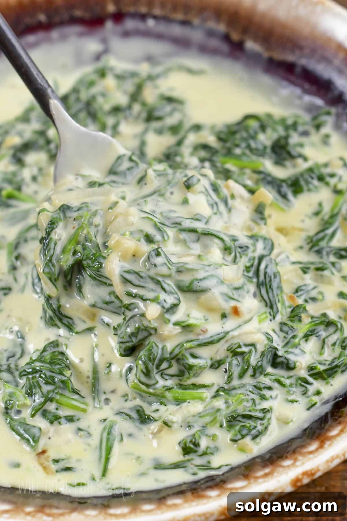 Decadent Cheesy Creamed Spinach 2 Closeup of a spoon scooping out creamy spinach from a bowl, highlighting its rich texture and vibrant green color.