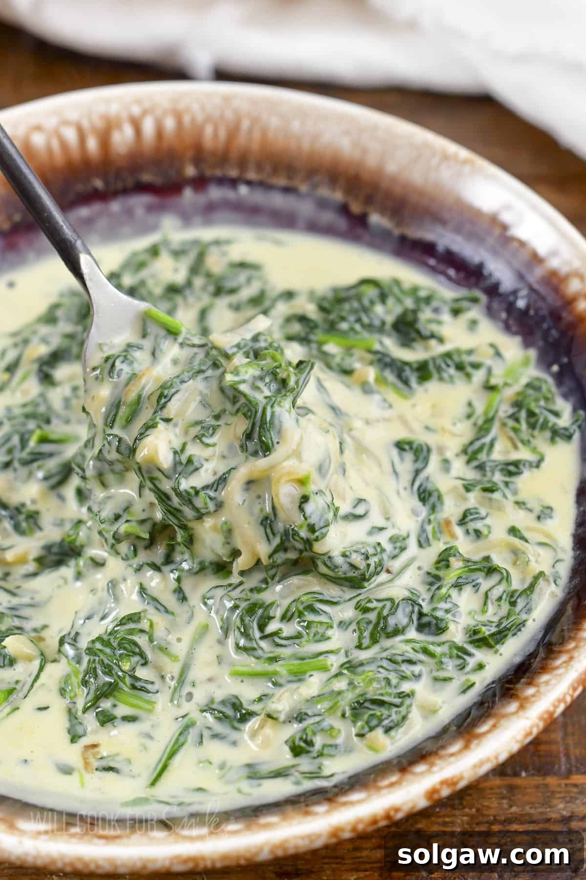 Decadent Cheesy Creamed Spinach 11 Scooping out a generous portion of creamy spinach from a serving bowl, showcasing its rich texture.