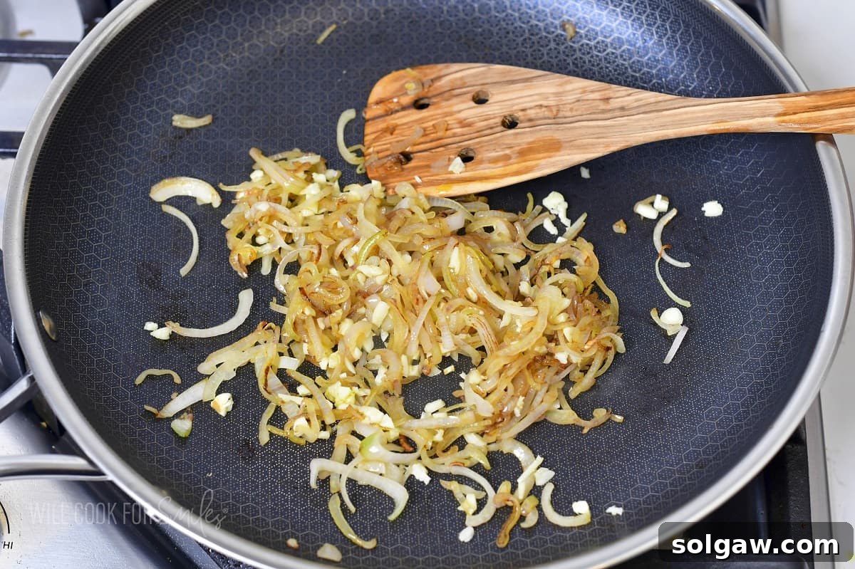 Decadent Cheesy Creamed Spinach 4 Sautéed shallots and garlic in a pan, stirred with a spatula, creating an aromatic base.