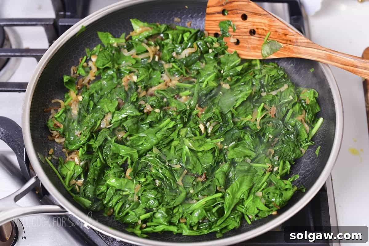 Decadent Cheesy Creamed Spinach 6 Cooked spinach mixed with onions in a large pan, ready for the creamy sauce.