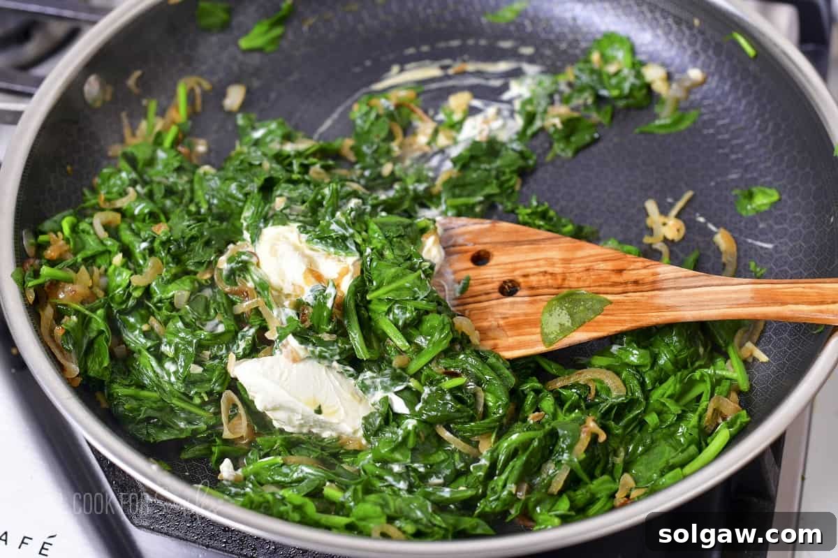 Decadent Cheesy Creamed Spinach 7 Stirring in cream cheese into the cooked spinach, creating a smooth, rich base.