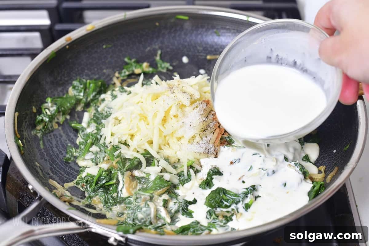 Decadent Cheesy Creamed Spinach 8 Adding heavy cream and a blend of cheeses to the spinach mixture in the pan.