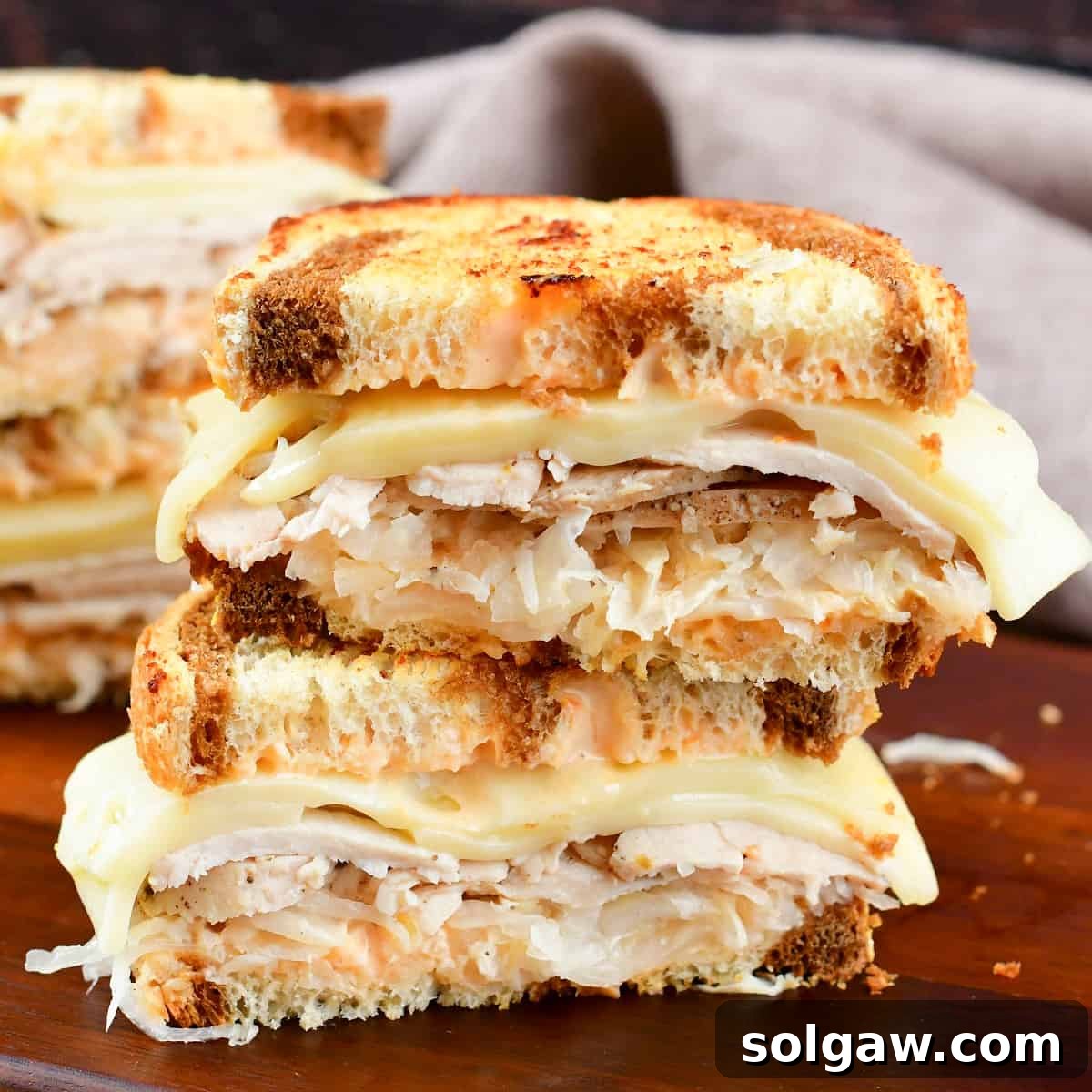 Closeup of two stacked halves of a perfectly grilled Turkey Reuben sandwich, showing the layers of filling and golden-brown bread.