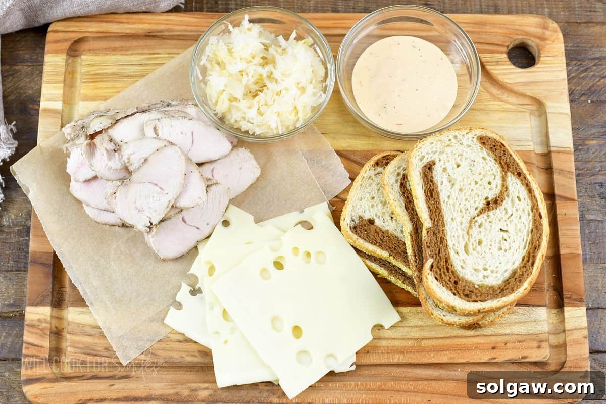 Turkey Reuben Melt 3 A cutting board filled with fresh ingredients for a Turkey Reuben sandwich, including rye bread, turkey slices, Swiss cheese, sauerkraut, and Thousand Island dressing.