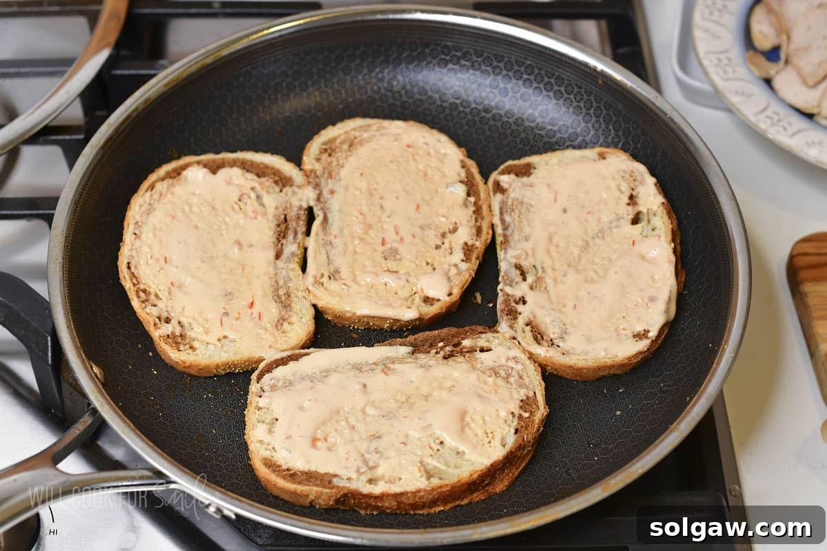 Turkey Reuben Melt 5 Four slices of rye bread arranged in a hot pan, two already spread with creamy Thousand Island dressing, ready for sandwich assembly.